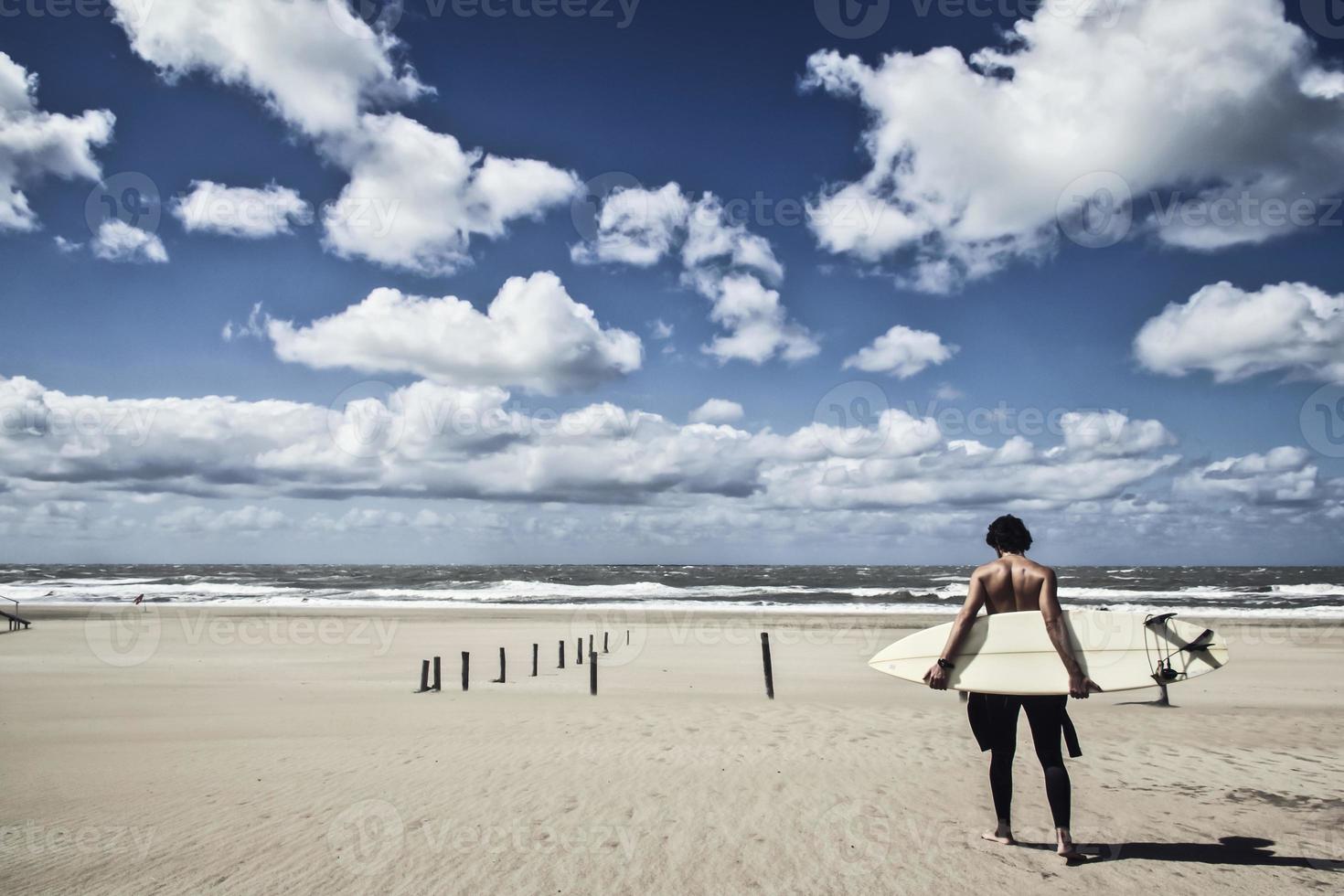 Young male surfer standing in the beach looking at the sea photo