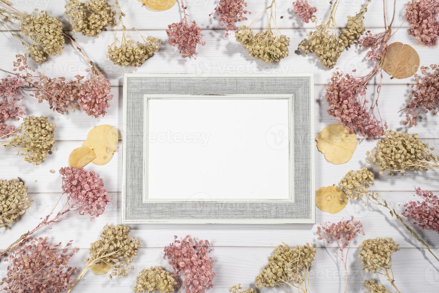 Top view of empty photo frame with dry colorful flowers over a white wooden table