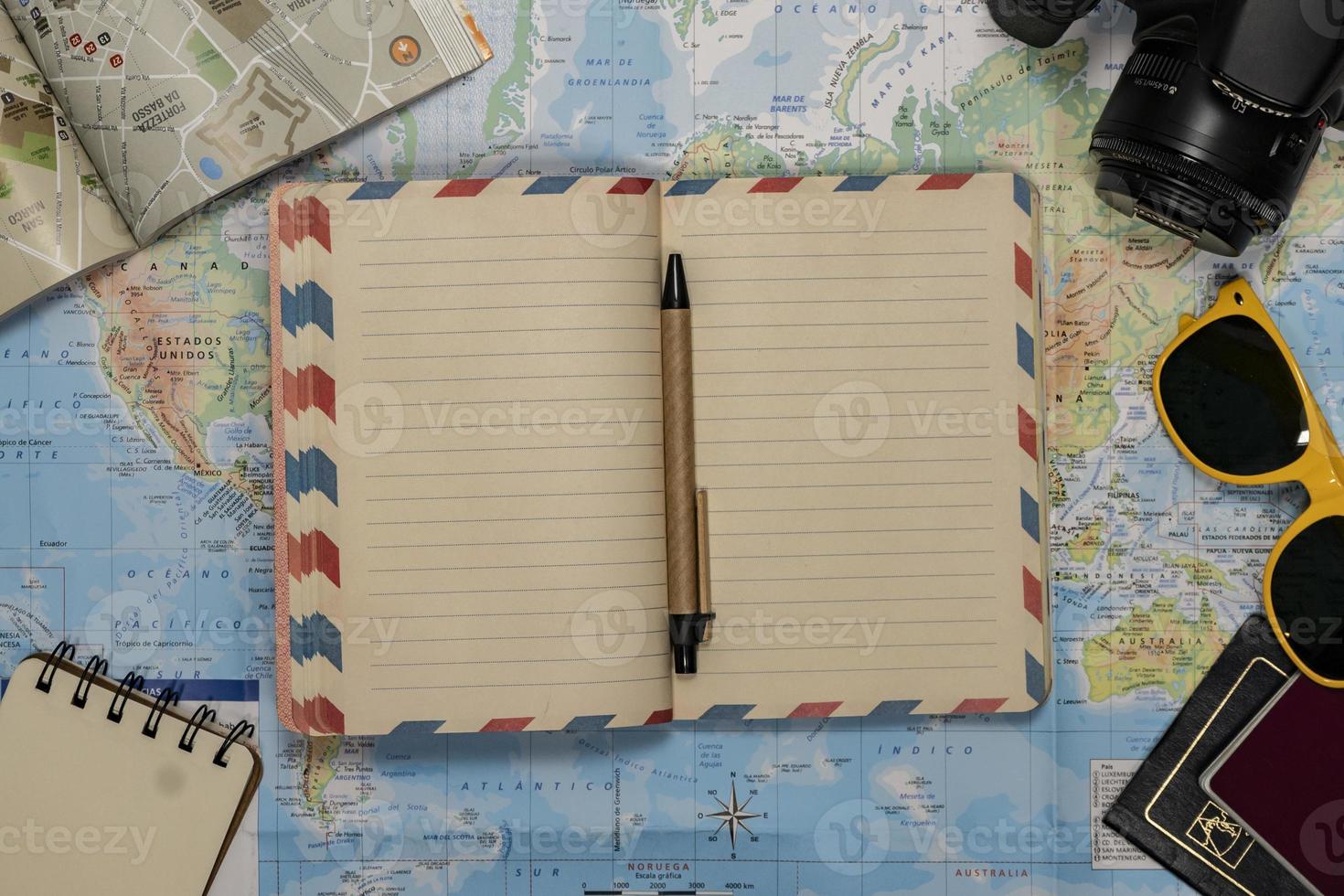 Travel Flat lay of an empty notebook, sunglasses, passport, camera over a world map photo