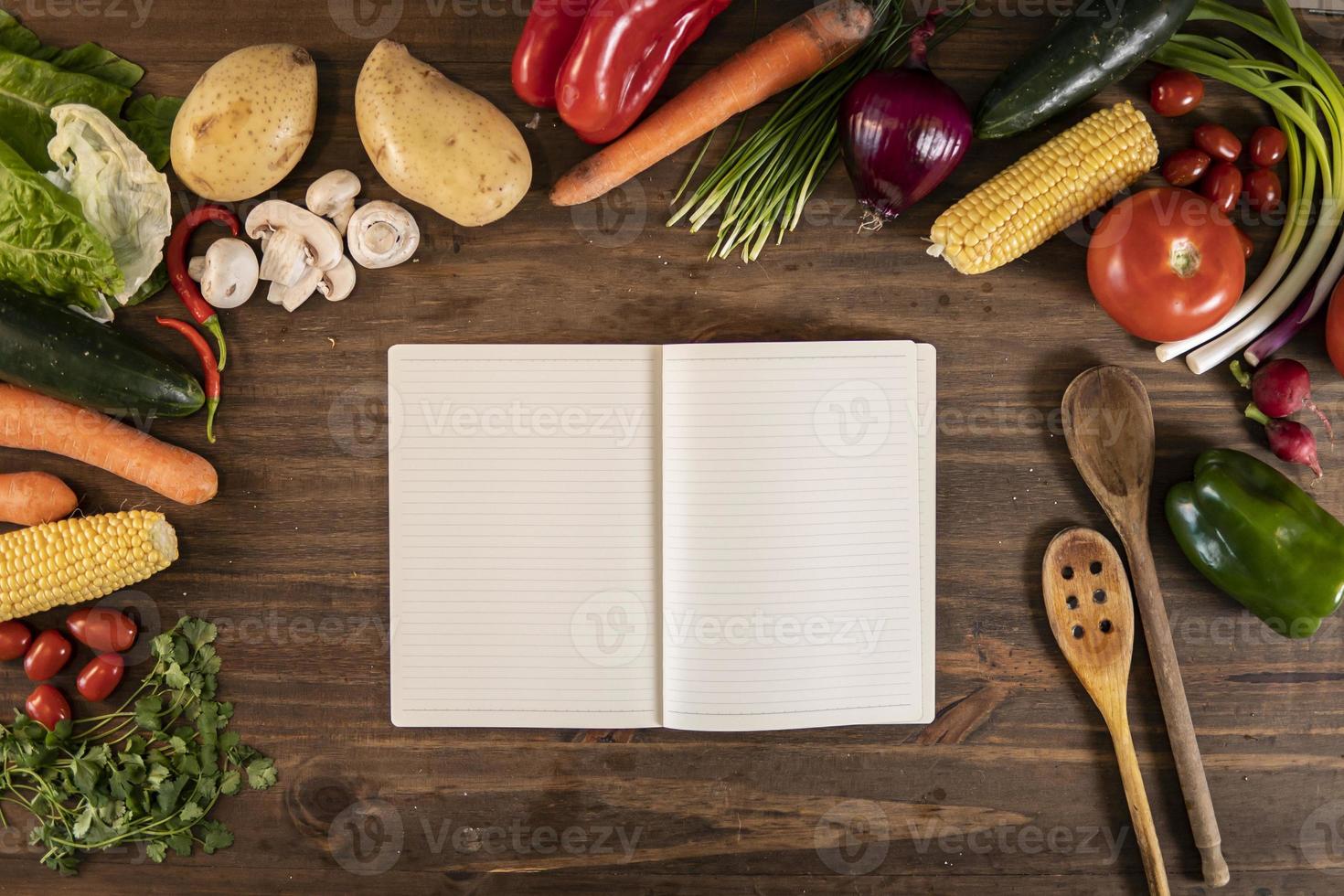 Flat lay of vegetables and food and an empty notebook over a wooden table photo