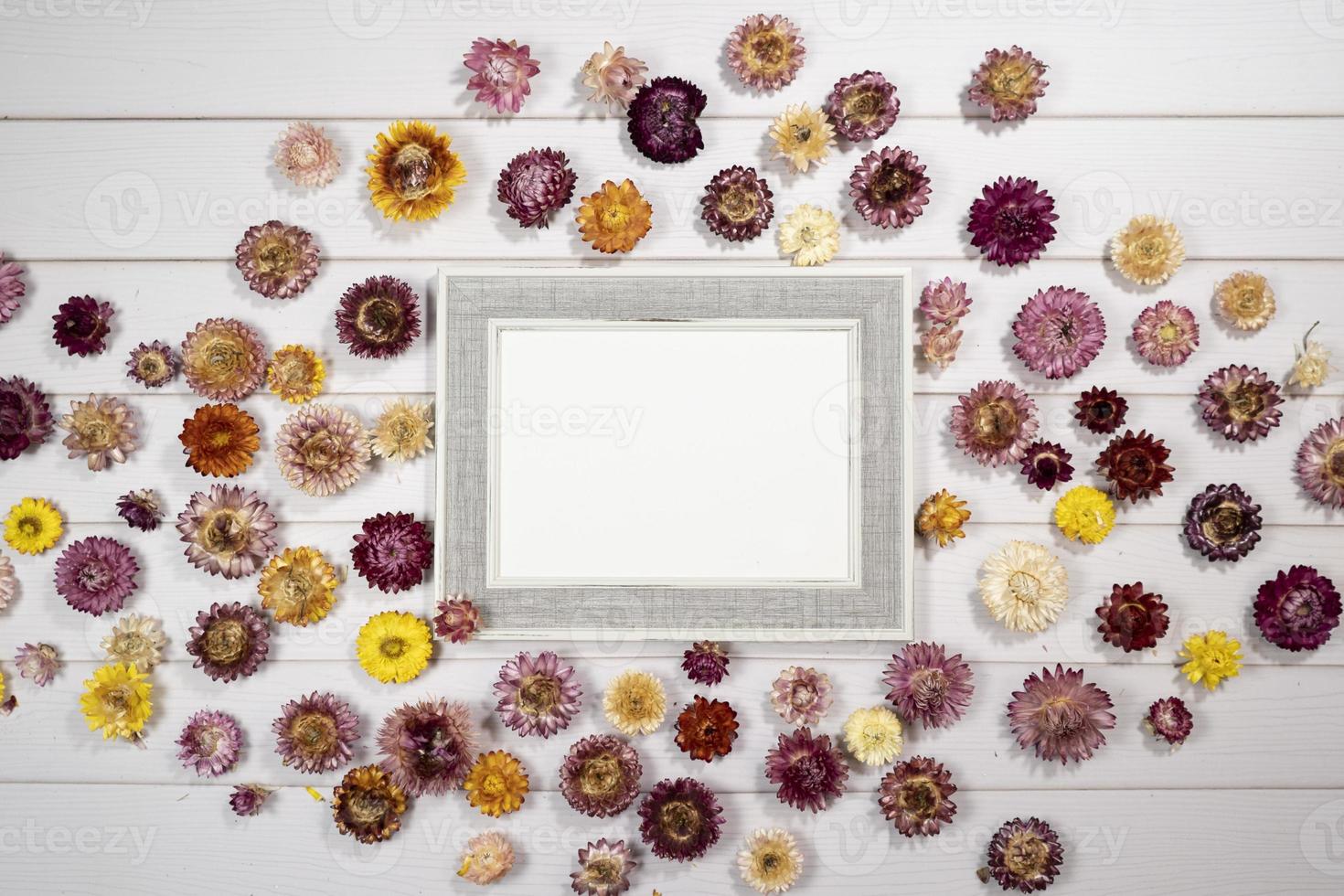 Top view of empty photo frame with dry colorful flowers over a white wooden table