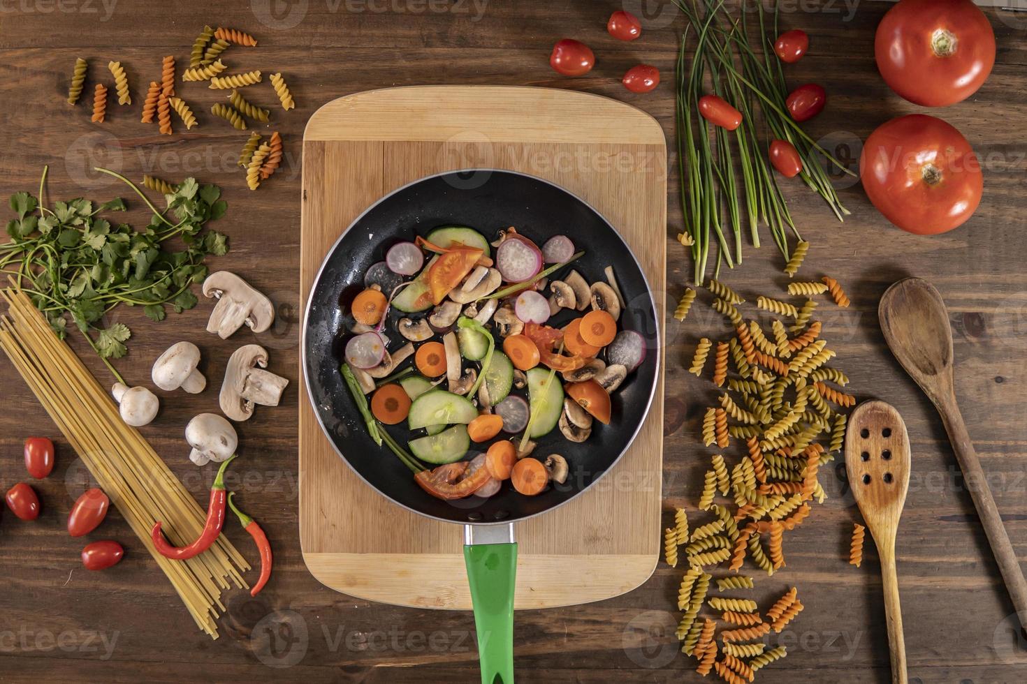 Flat lay of vegetables and food and a frying pan with food over a wooden table photo