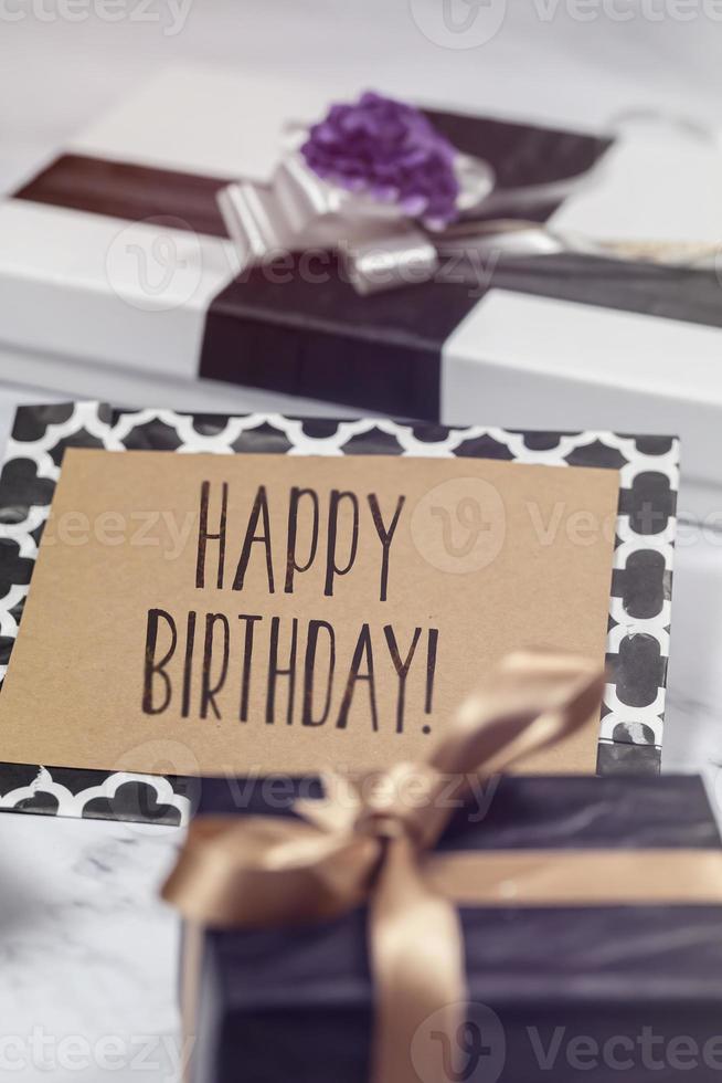 Happy Birthday card with gifts and presents over white marble table, black, white, violet and gold colors photo