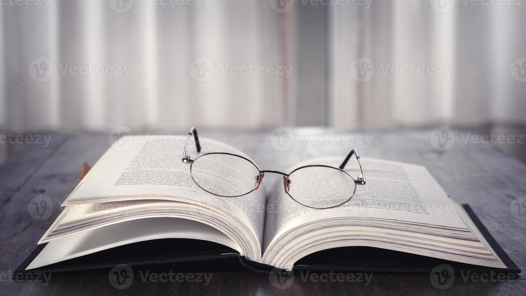 abierto libro terminado de madera mesa con lentes en él. biblioteca. literatura. leer. estudiar foto