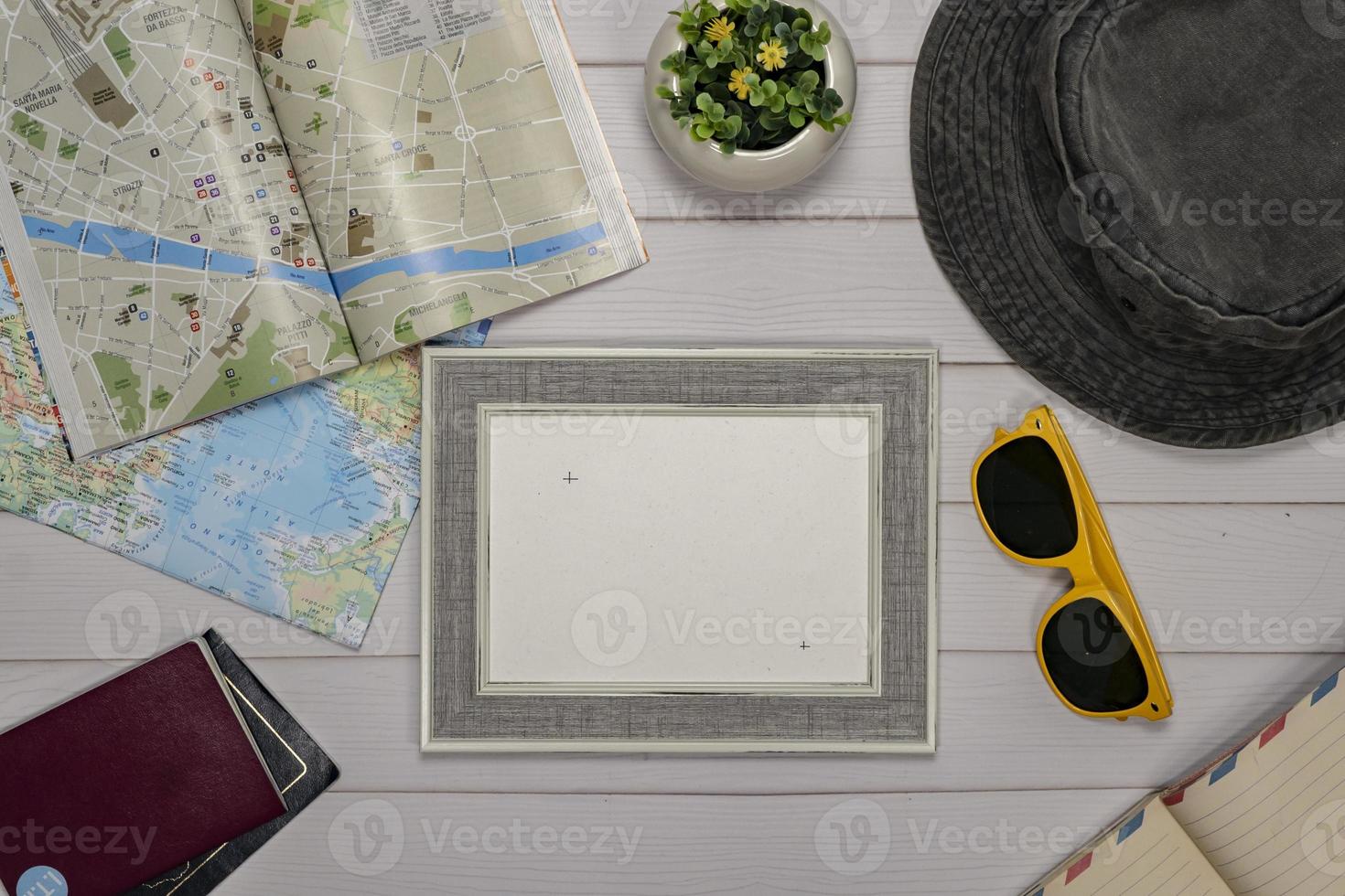 Travel Flat lay of an empty frame, sunglasses, passport, camera and a map over a white wooden table photo