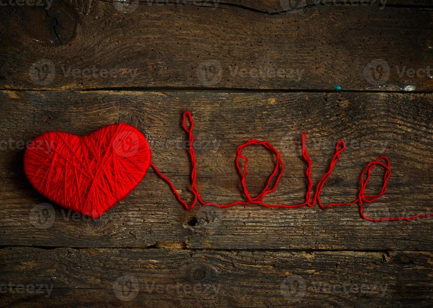 Red heart shape with an inscription love made from wool on old shabby wooden background photo