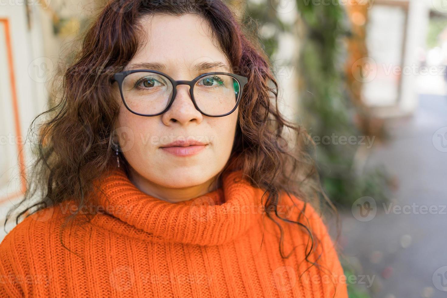 Portrait of carefree young woman smiling with urban background. Cheerful latin girl wearing eyeglasses in the city. Happy brunette woman with curly hair and spectacles smiling. photo