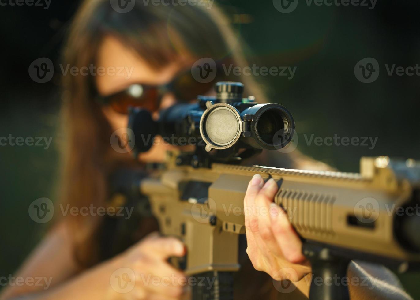 Girl with a gun for trap shooting and shooting glasses aiming at a target photo