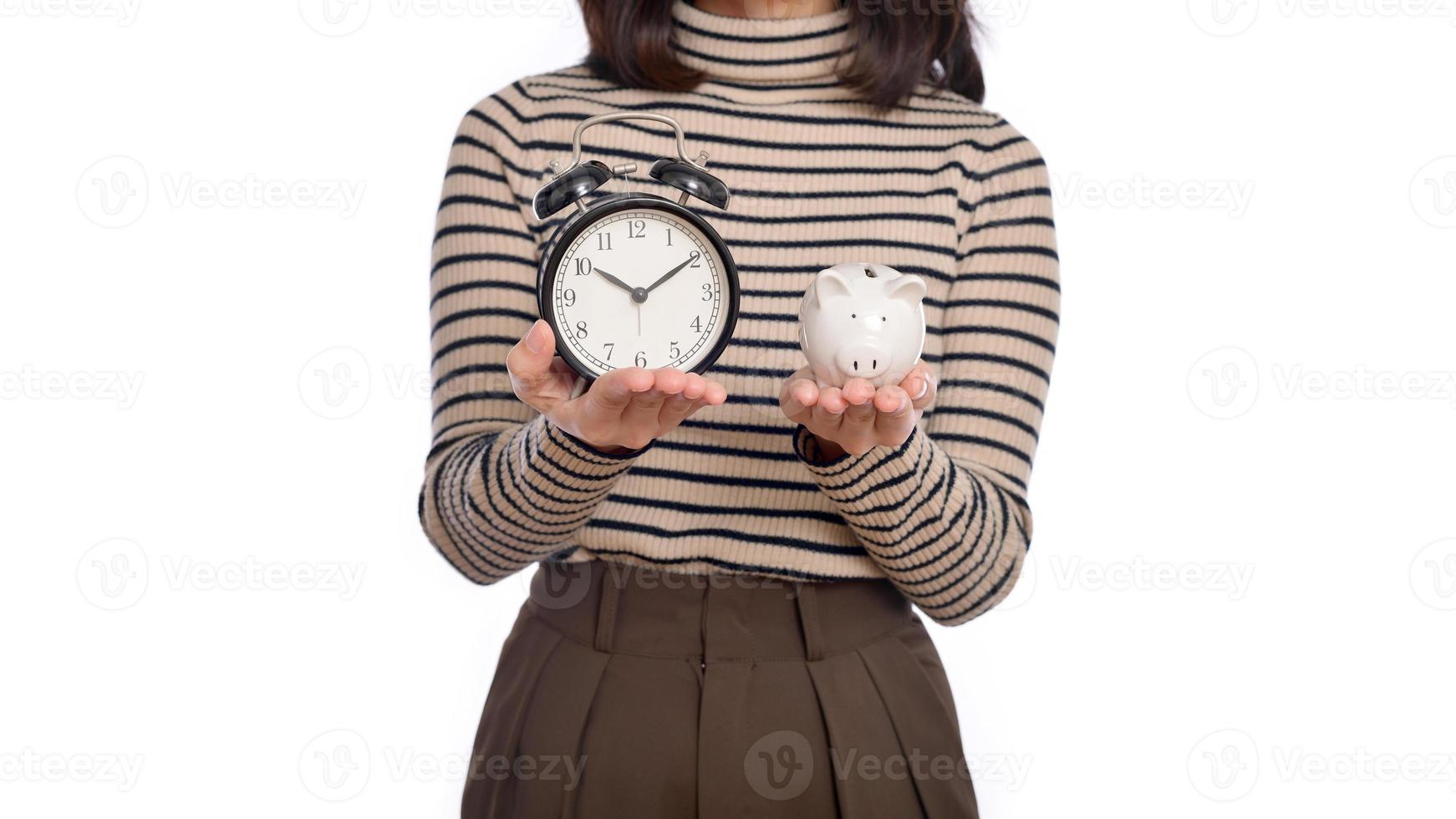 Portrait of young Asian woman casual uniform holding white piggy bank and alarm clock isolated on white background, Financial and bank saving money concept photo