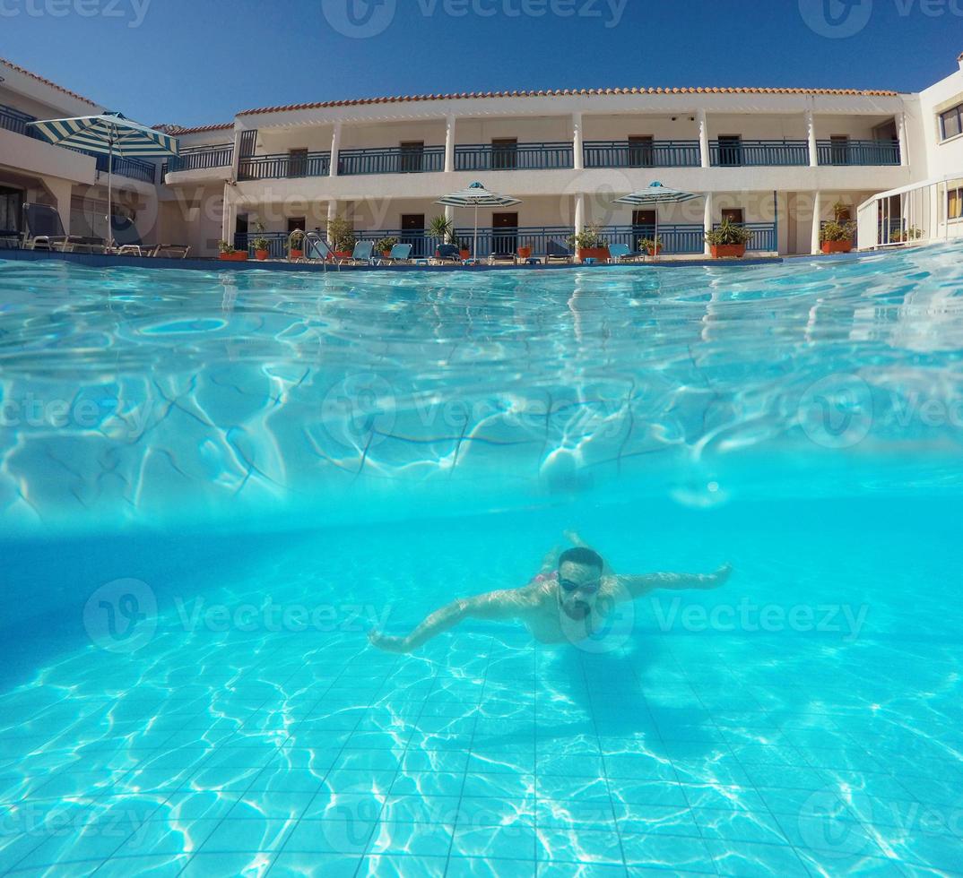 Beard man with glasses swimming under water in the pool on a tropical resort photo