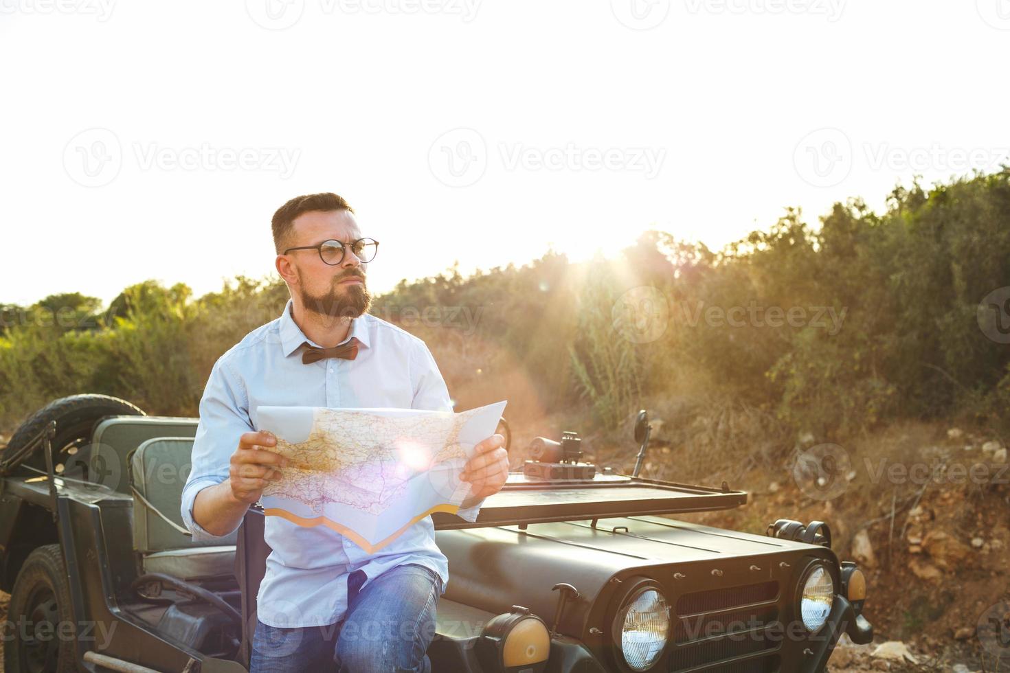 joven elegante hombre con lentes y arco Corbata ver el mapa cerca el Anticuado suv foto