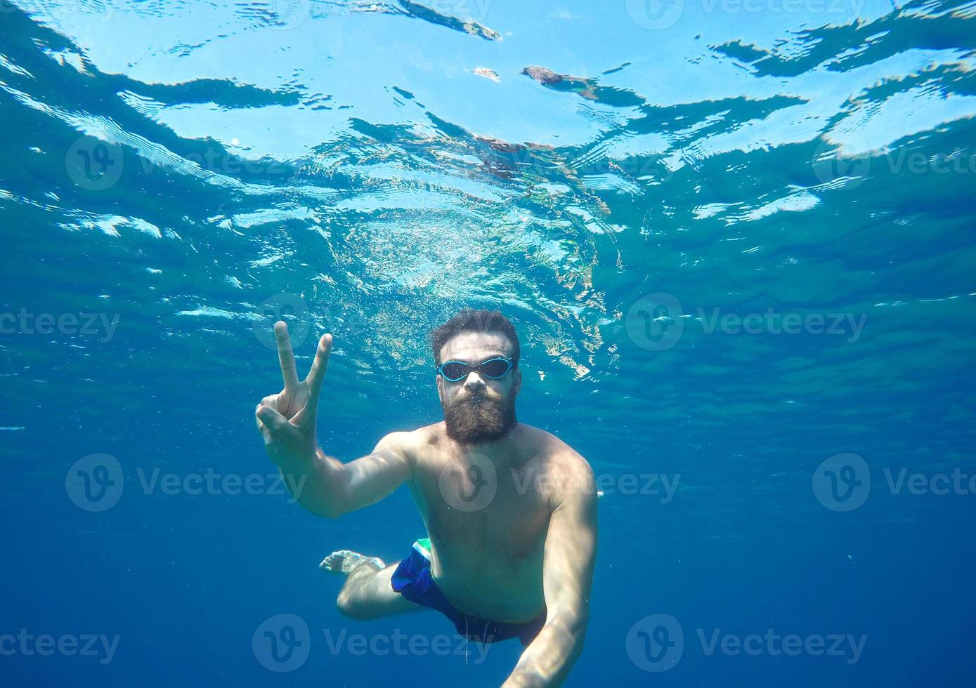 Man doing underwater selfie shot with selfie stick in blue sea photo