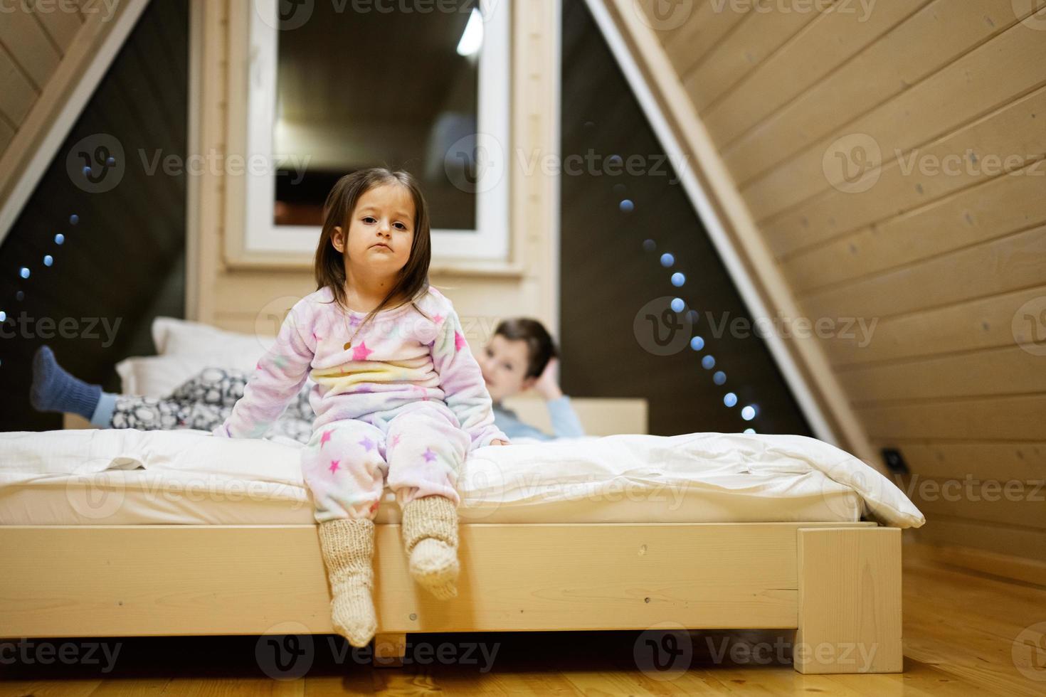 Children in soft warm pajamas playing at wooden cabin home. Concept of childhood, leisure activity, happiness. Brother and sister having fun and playing together. photo