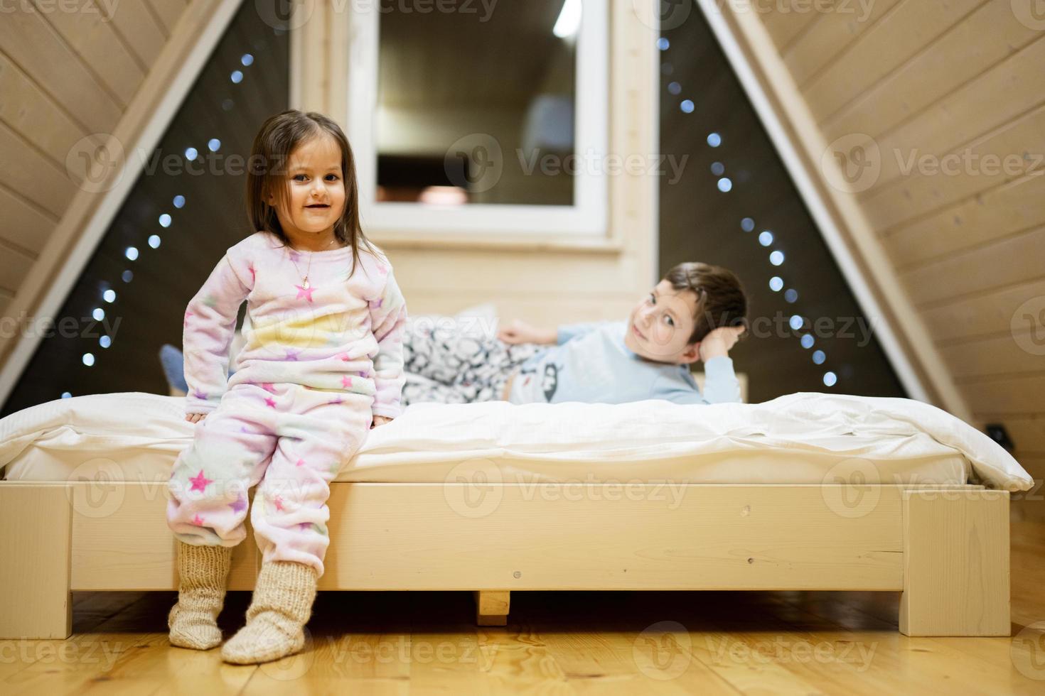 Children in soft warm pajamas playing at wooden cabin home. Concept of childhood, leisure activity, happiness. Brother and sister having fun and playing together. photo