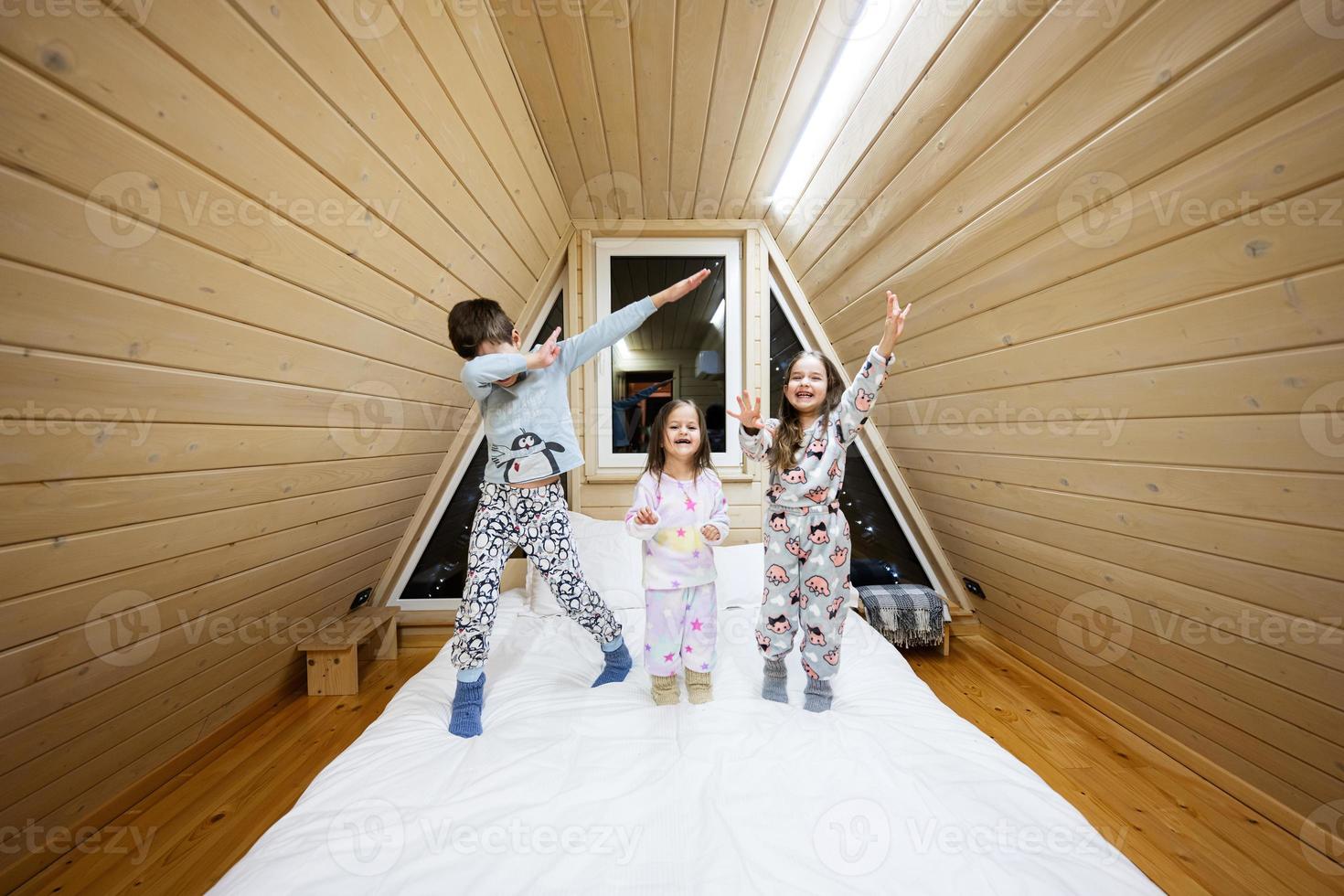 Children in soft warm pajamas playing at wooden cabin home. Concept of childhood, leisure activity, happiness. Brother and sisters having fun and playing together. photo