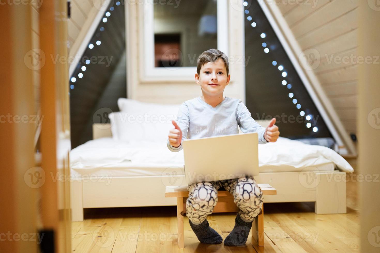 Boy in pajama sit with laptop at wooden cabin home. Concept of childhood, leisure activity, happiness. photo