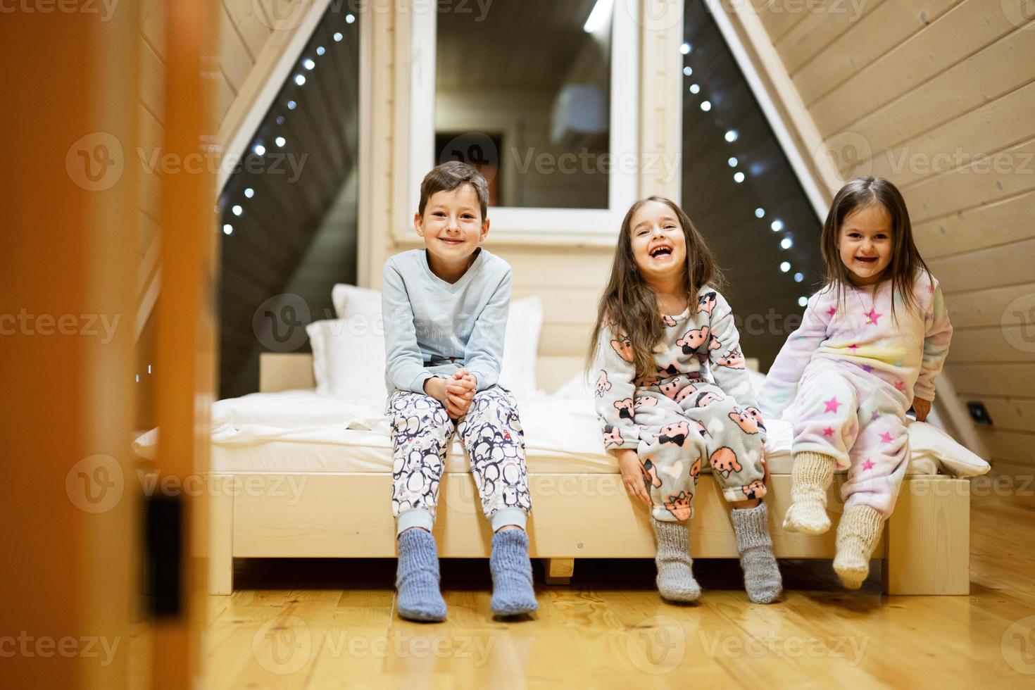 Children in soft warm pajamas playing at wooden cabin home. Concept of childhood, leisure activity, happiness. Brother and sisters having fun and playing together. photo