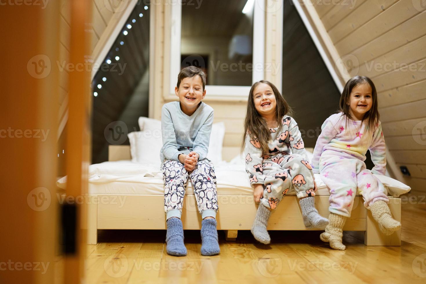 Children in soft warm pajamas playing at wooden cabin home. Concept of childhood, leisure activity, happiness. Brother and sisters having fun and playing together. photo