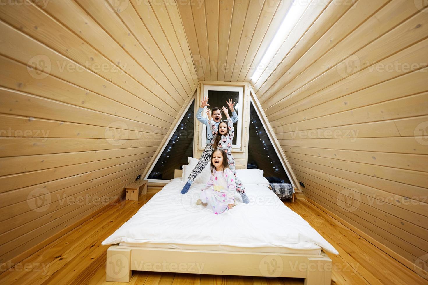 Children in soft warm pajamas playing at wooden cabin home. Concept of childhood, leisure activity, happiness. Brother and sisters having fun and playing together. photo