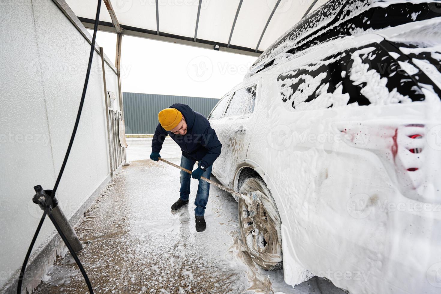 Man washing american SUV car with mop at a self service wash in cold weather. photo