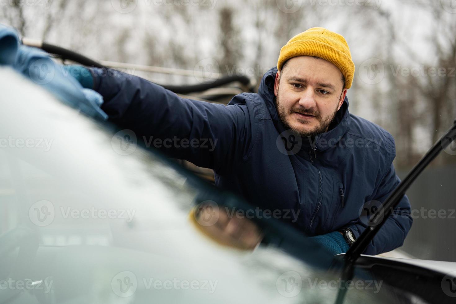 Man wipes american SUV car windshield with a microfiber cloth after washing in cold weather. photo