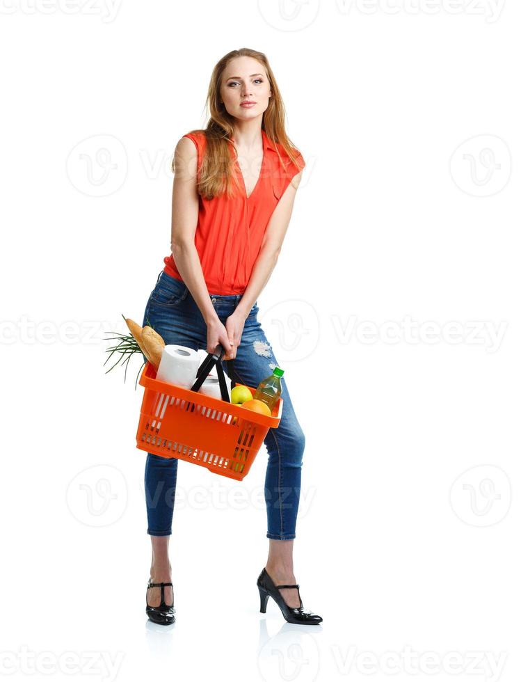 Happy young woman holding a basket full of healthy food on white. Shopping photo