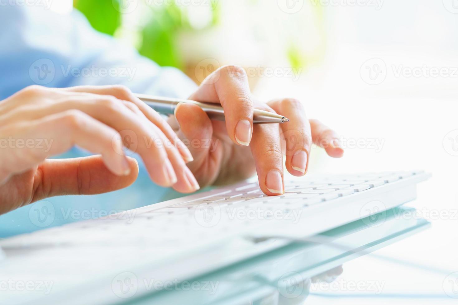 mujer oficina trabajador con bolígrafo en mano mecanografía en el teclado foto