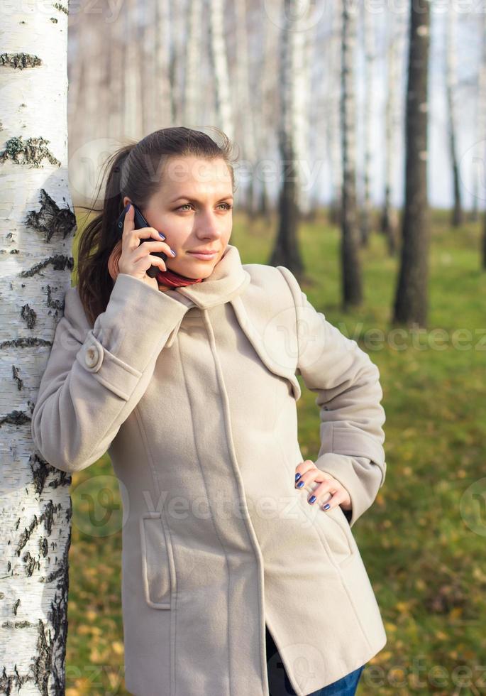 Portrait of a girl under the birch with phone photo