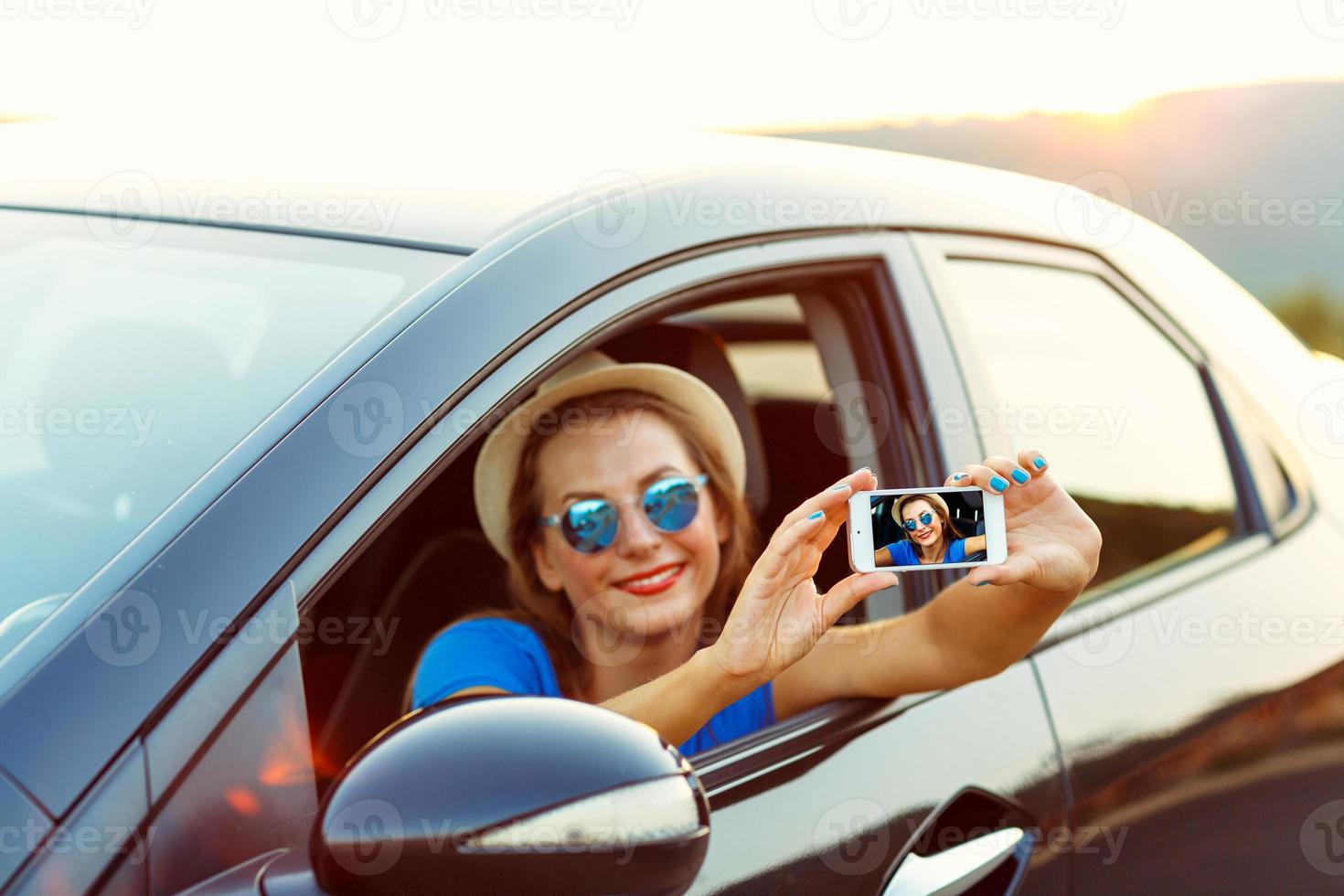 Woman in hat and sunglasses making self portrait sitting in the car photo