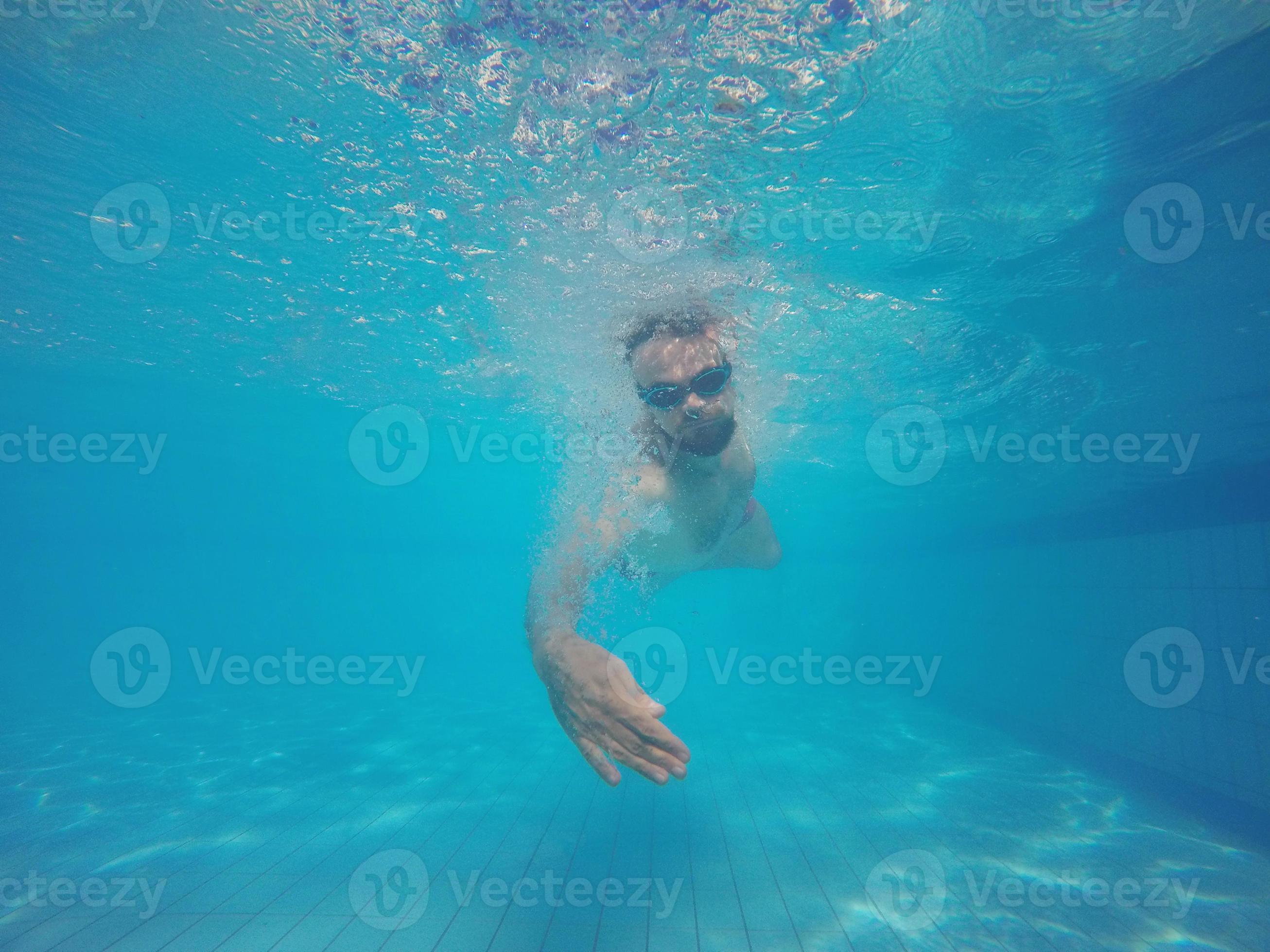 Hombre con gafas de natación buceando en piscina