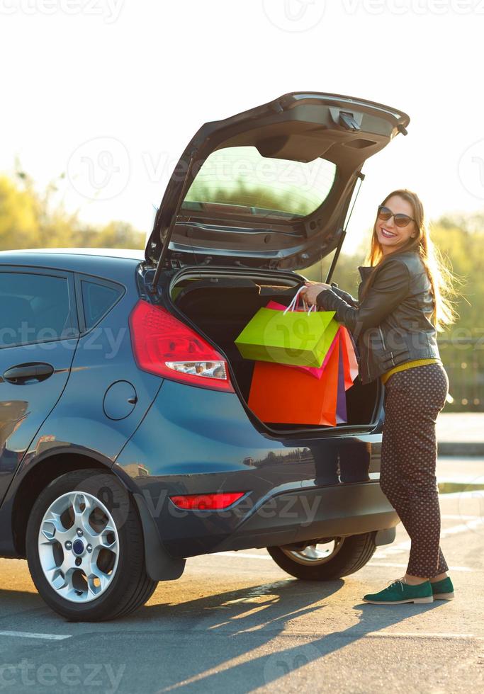 sonriente caucásico mujer poniendo su compras pantalones dentro el coche maletero foto