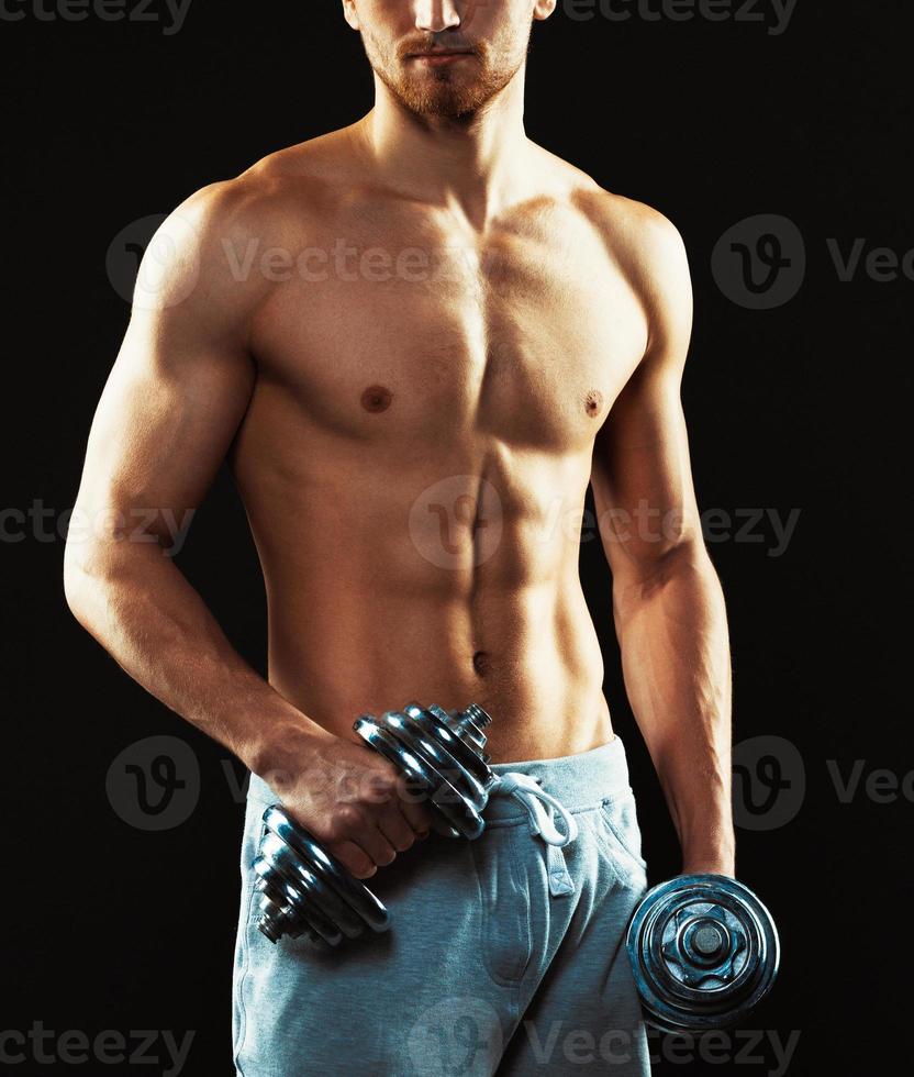 Athletic man with dumbbells on the black photo