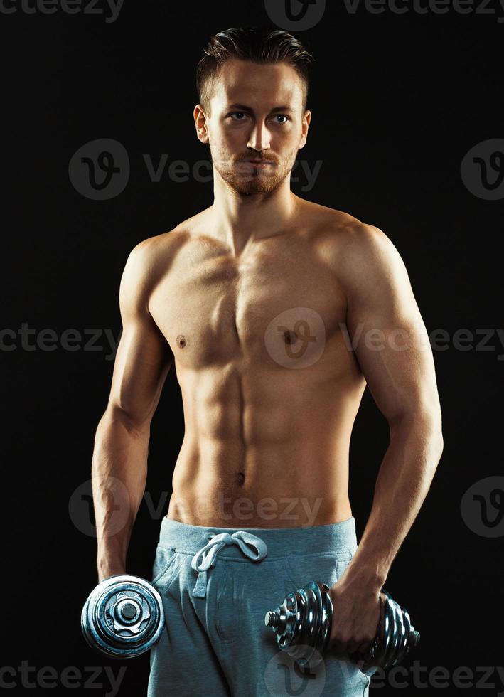 Athletic attractive man with dumbbells on the black photo