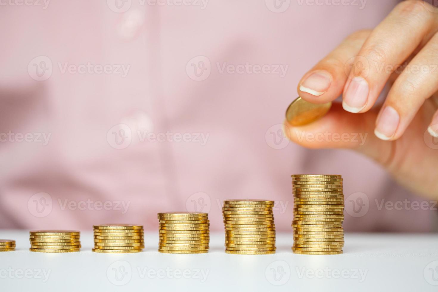 Female hand stacking gold coins into increasing columns photo