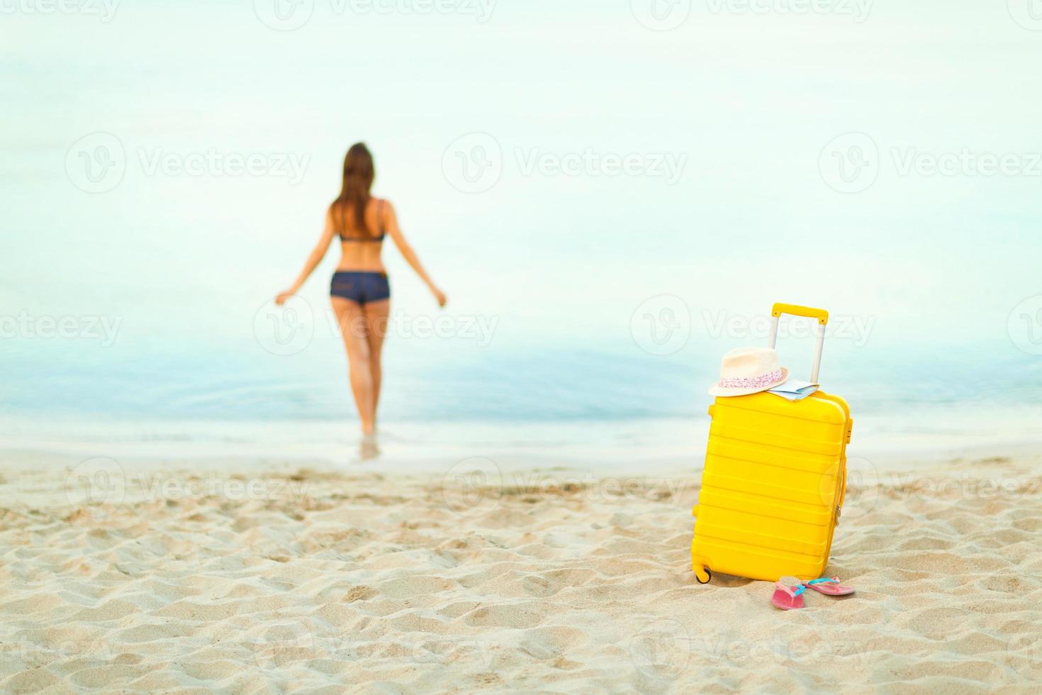 Yellow suitcase on the beach and a girl walks into the sea in the background photo