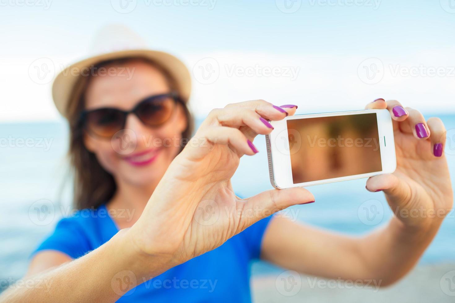 Girl in the hat making selfie by the smartphone on the background of sea coast, Adriatic sea photo