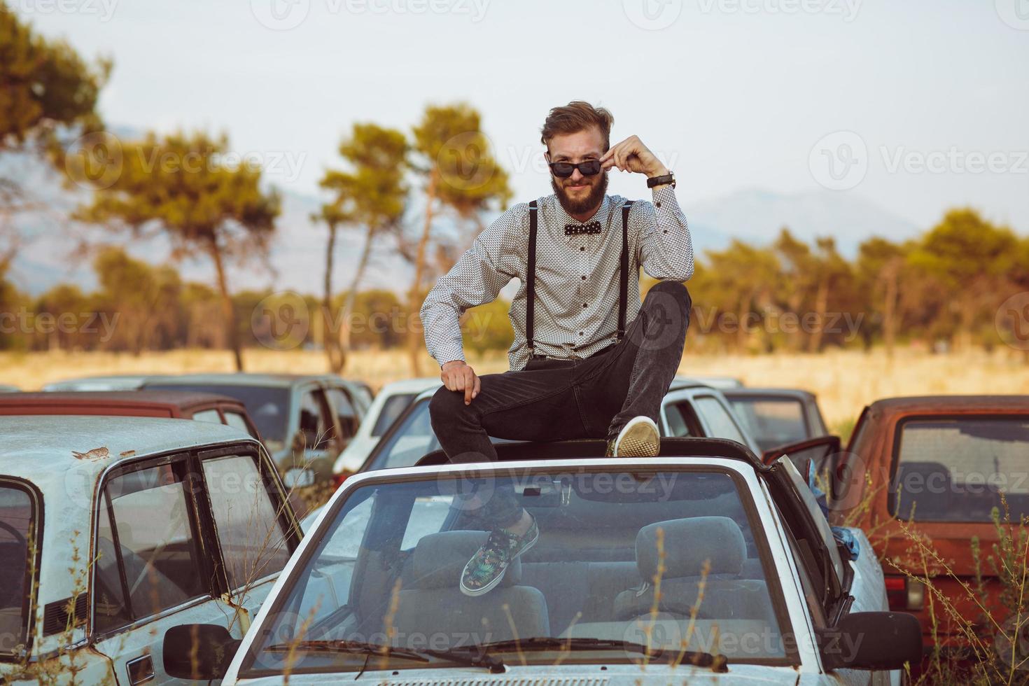 Young handsome stylish man, wearing shirt and bow-tie on the field of old cars photo