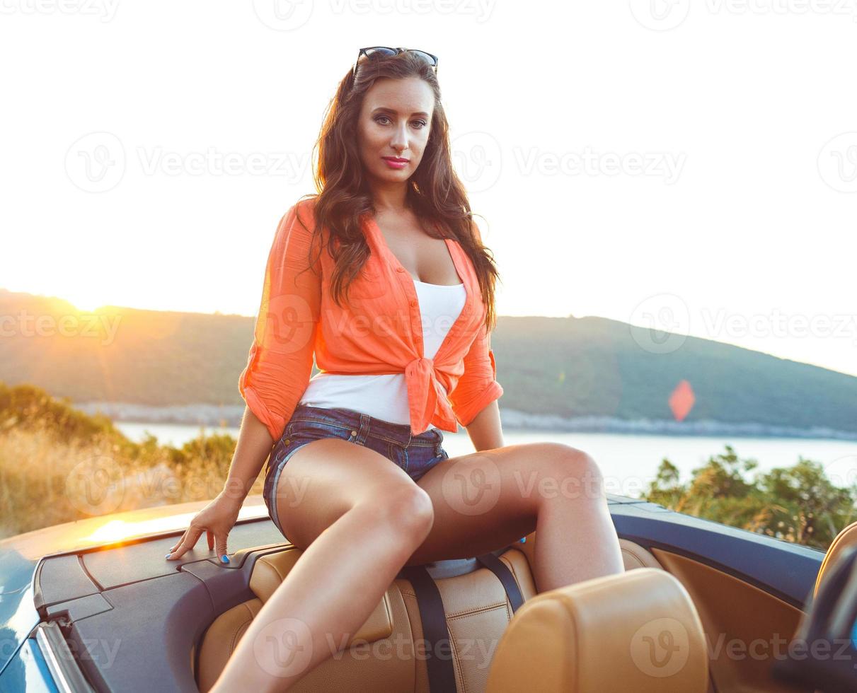 Beautiful woman sitting in cabriolet, enjoying trip on luxury modern car with open roof photo