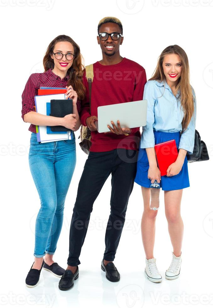 contento estudiantes en pie y sonriente con libros, ordenador portátil y pantalones aislado en blanco foto