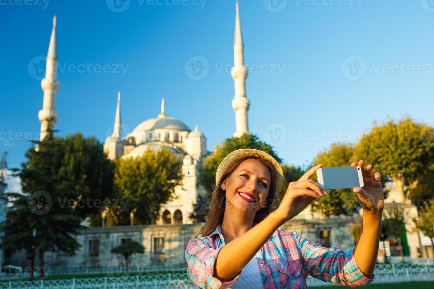 niña en el sombrero haciendo selfie por el teléfono inteligente en el antecedentes de el azul mezquita, Estanbul foto