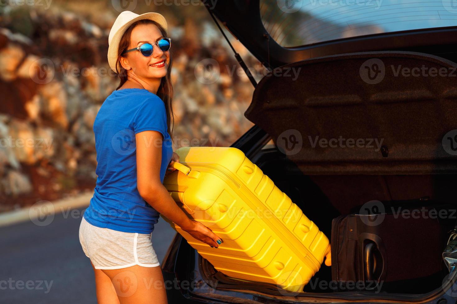 Young woman loading luggage into the back of car photo