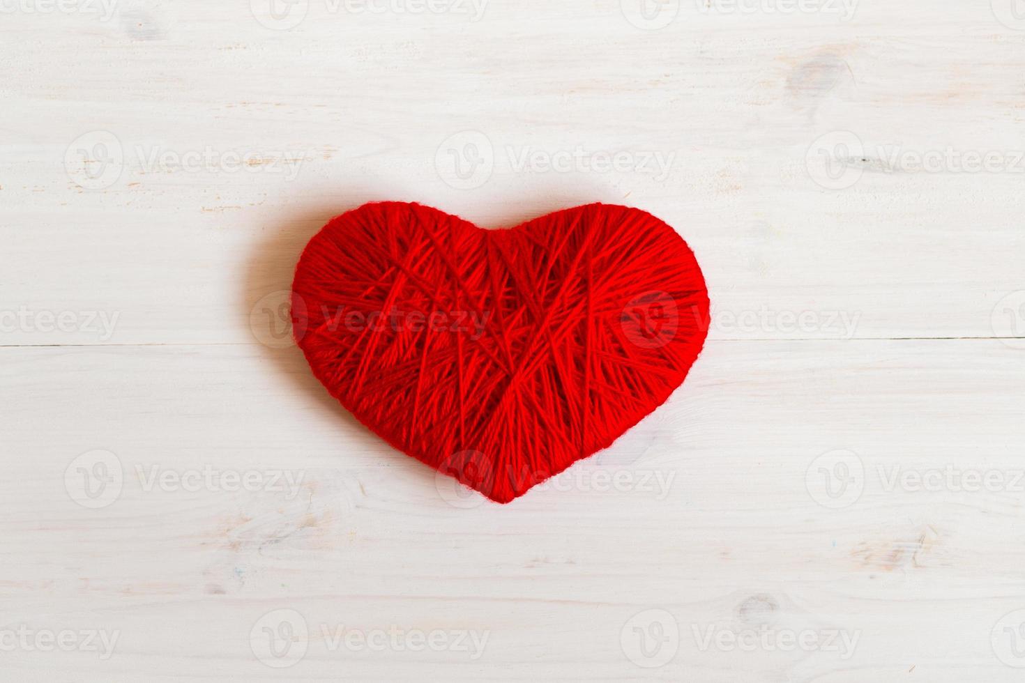 Red heart shape made from wool on white wooden background photo