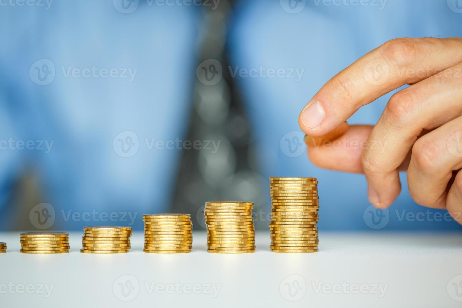 Male hand stacking gold coins into increasing columns photo