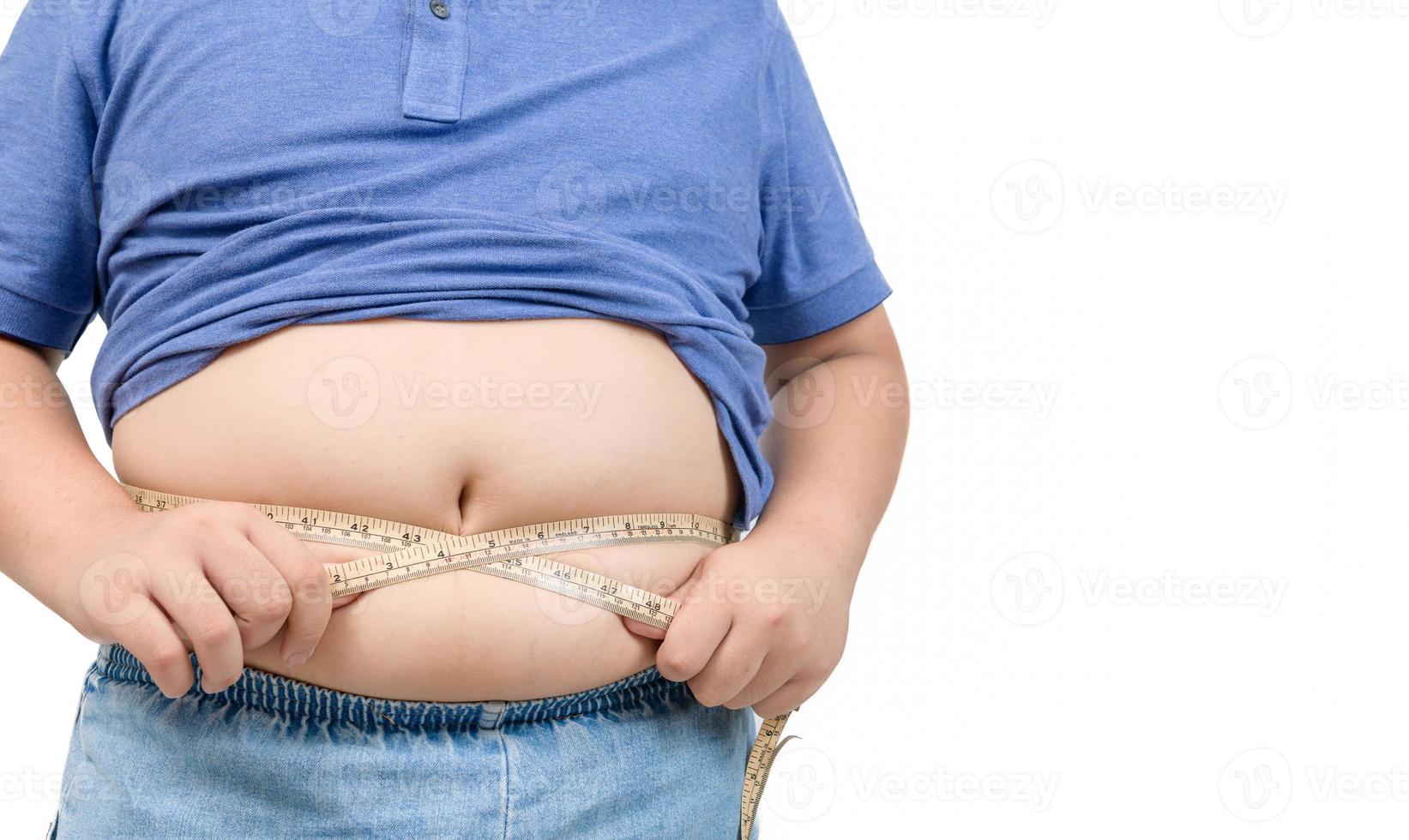 Obese boy measures his fat belly with a measuring tape isolated on white photo