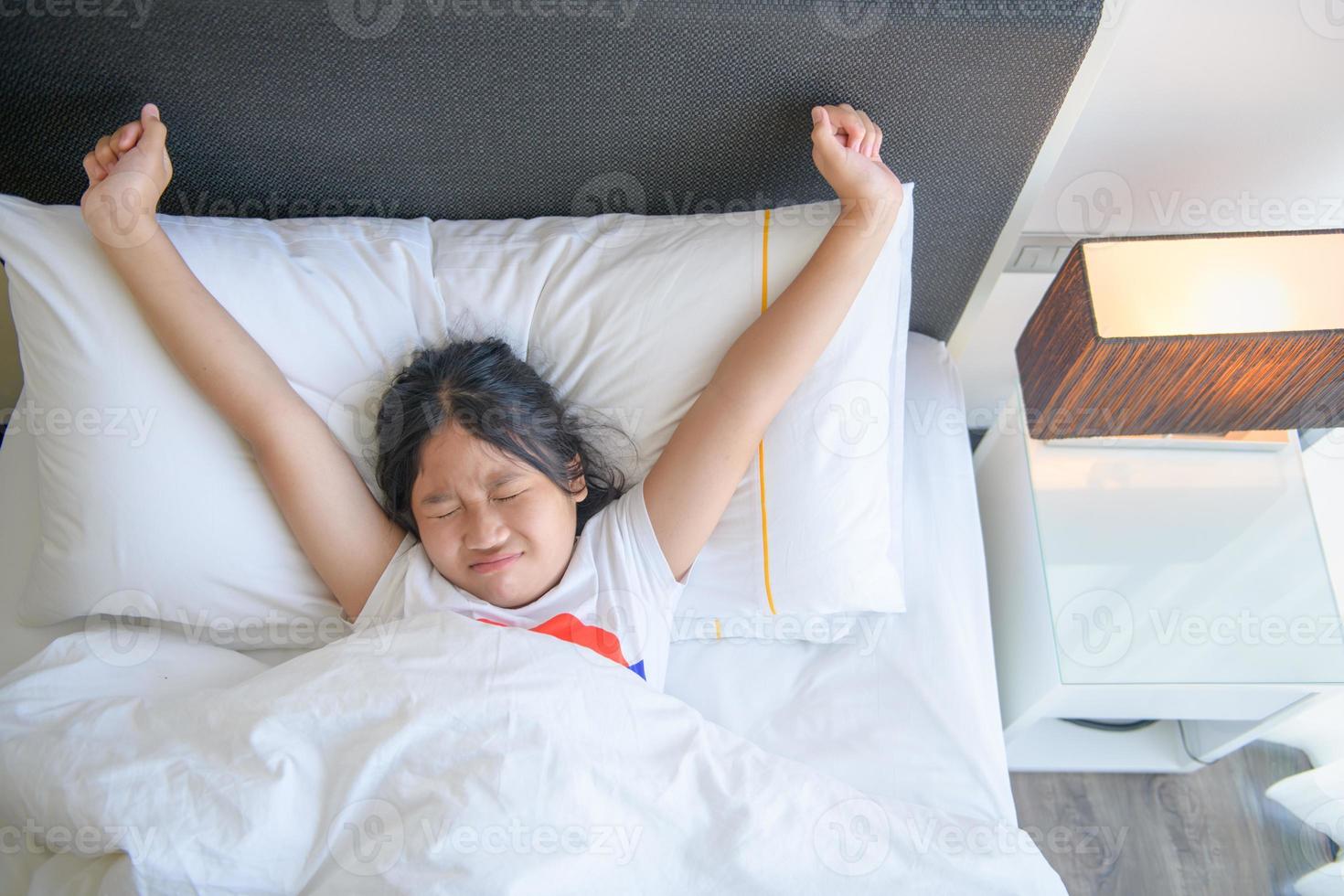 Cute little girl stretching her arms happily from waking up in her bed. photo