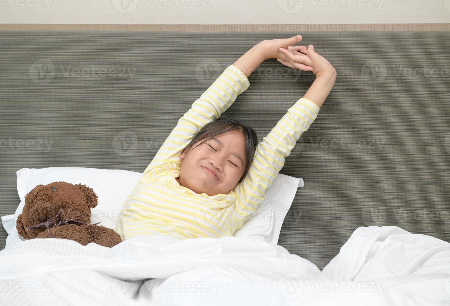 Lazy little girl wakes up and stretching on bed in morning, Health care and good morning photo