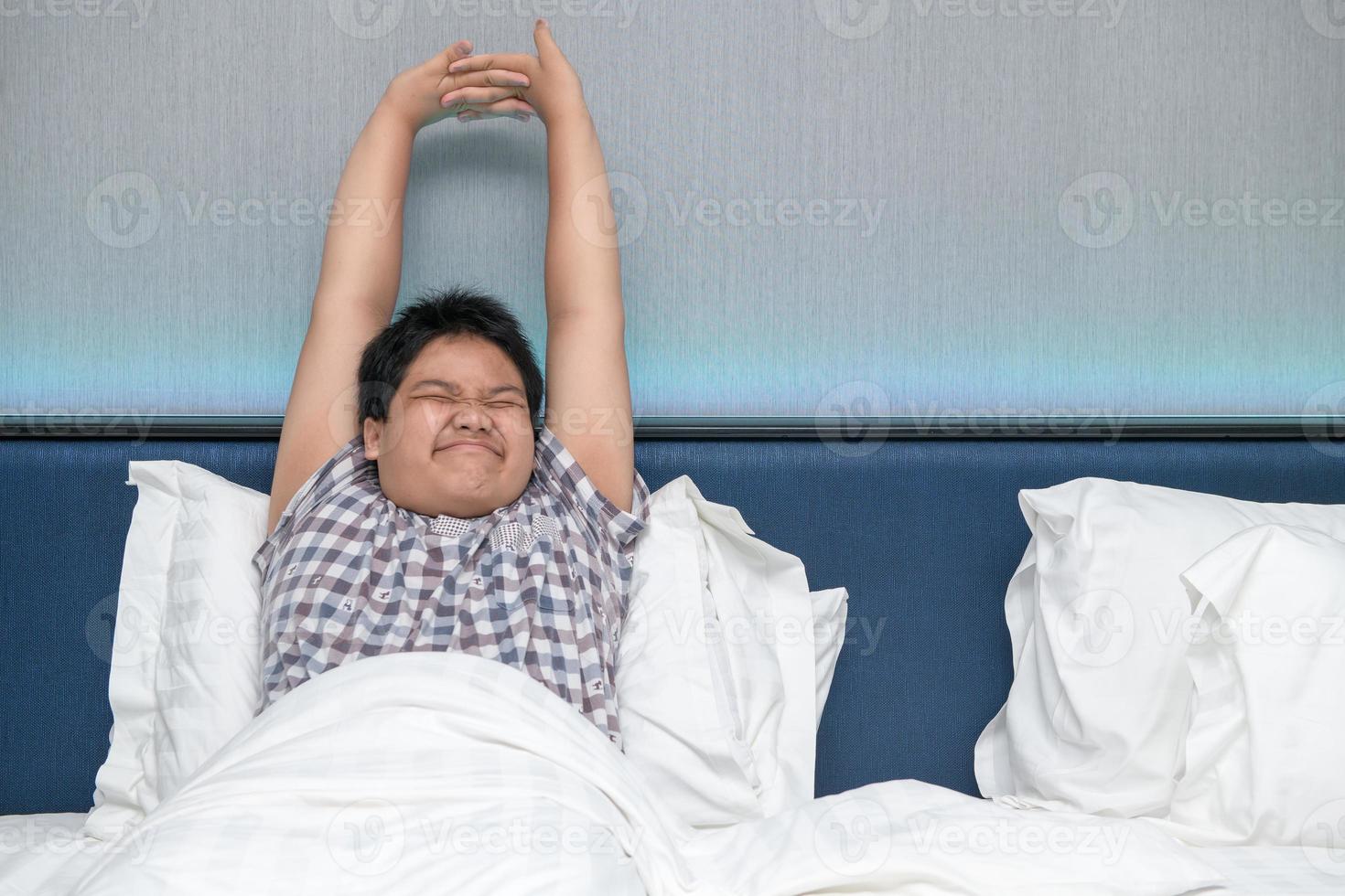 Obese fat boy waking up in bed and stretching his arms in the morning photo