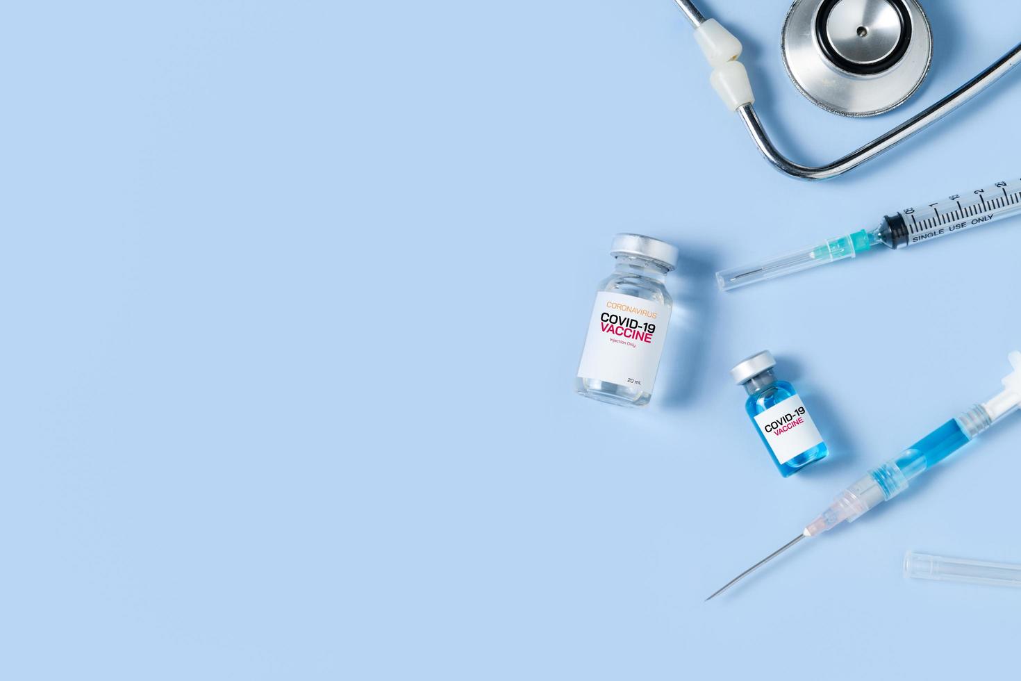 A vial of the Covid 19 vaccine with syringe and stethoscope on blue background, photo