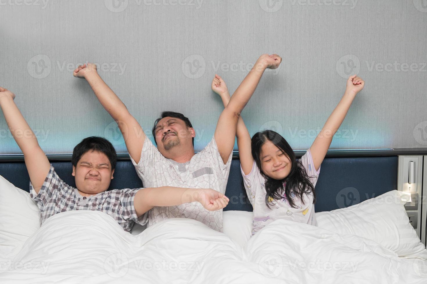 Happy family wake up in morning stretching hand rise up to the air while sitting on bed in bedroom photo