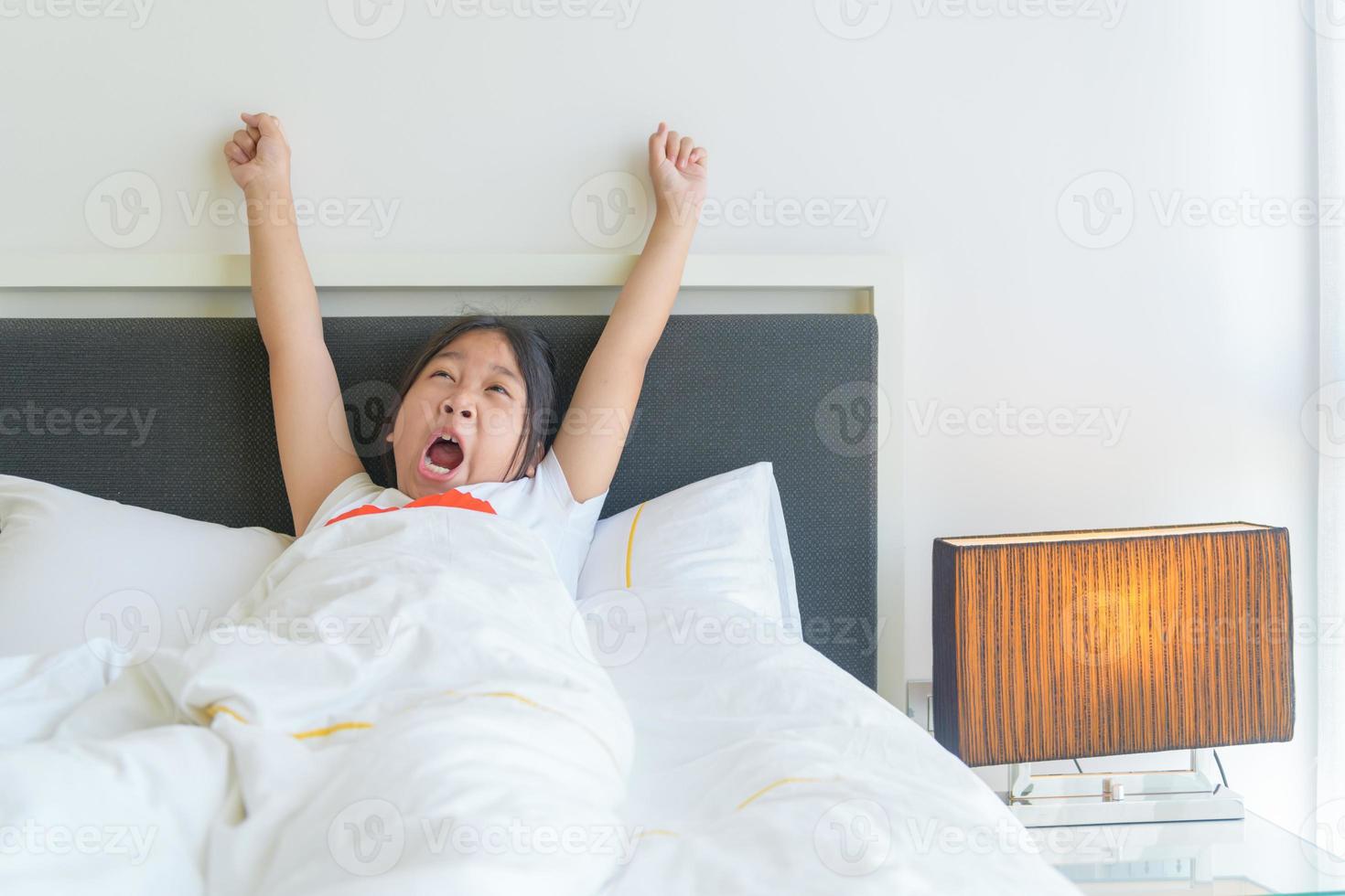 Cute little girl stretching her arms and yawn on bed. photo